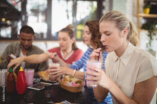 Young woman drinking milkshake with friends at cafe