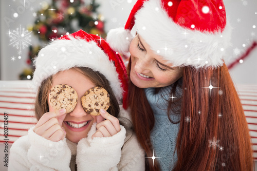 Festive mother and daughter on the couch with cookies against snow falling