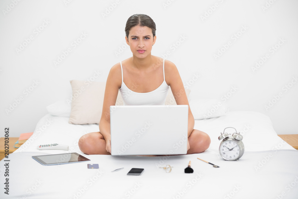 Irritated young brown haired model in white pajamas holding a laptop Irritated young brown haired model in white pajamas holding a laptop