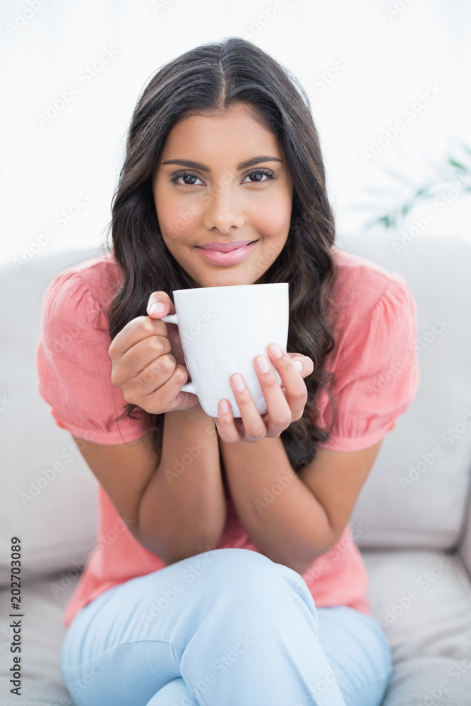 Content cute brunette sitting on couch holding mug
