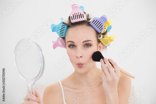 Funny natural brown haired woman in hair curlers applying powder on her face