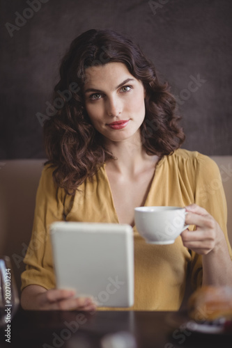 Woman holding coffee cup and digital tablet in restaurant