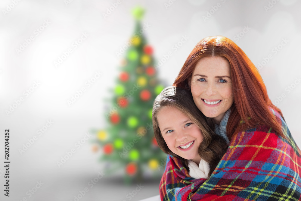 Mother and daughter under blanket against blurry christmas tree in room Mother and daughter under blanket against blurry christmas tree in room