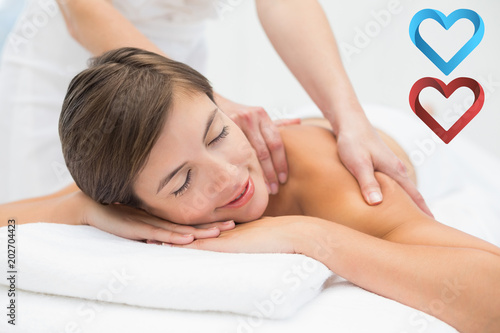 Attractive young woman receiving shoulder massage at spa center against hearts