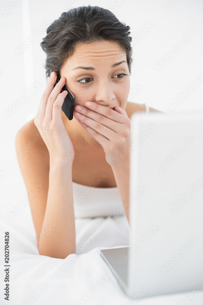 Surprised casual brunette in white pajamas making a phone call Surprised casual brunette in white pajamas making a phone call