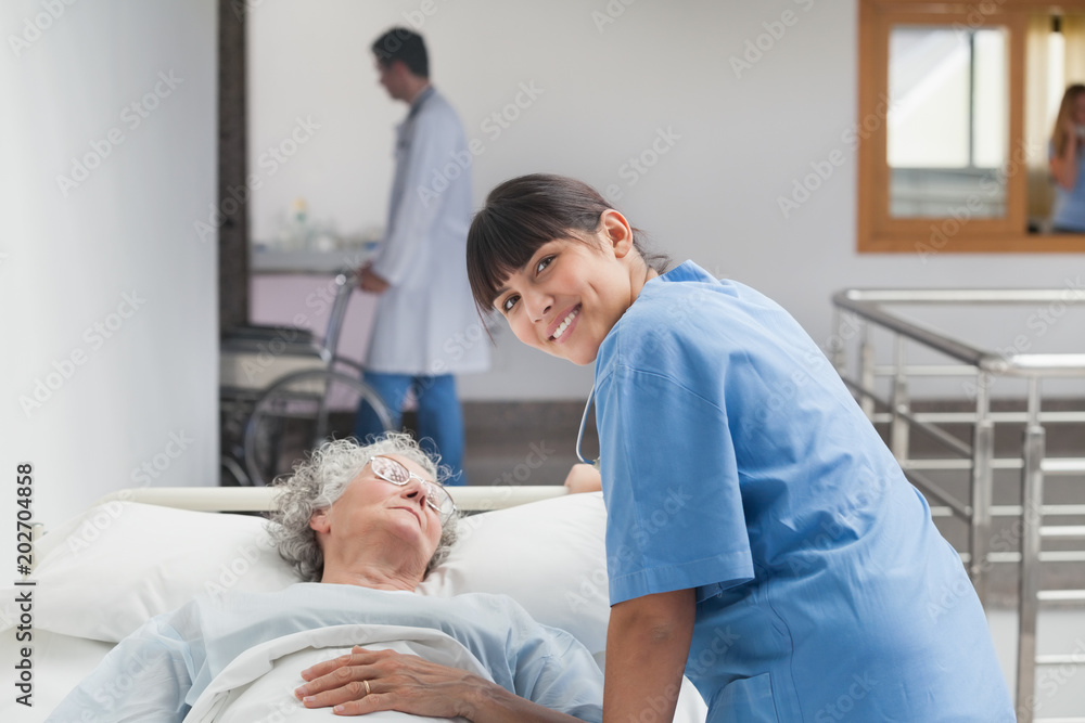 Obraz premium Smiling nurse leaning on the bed of a patient