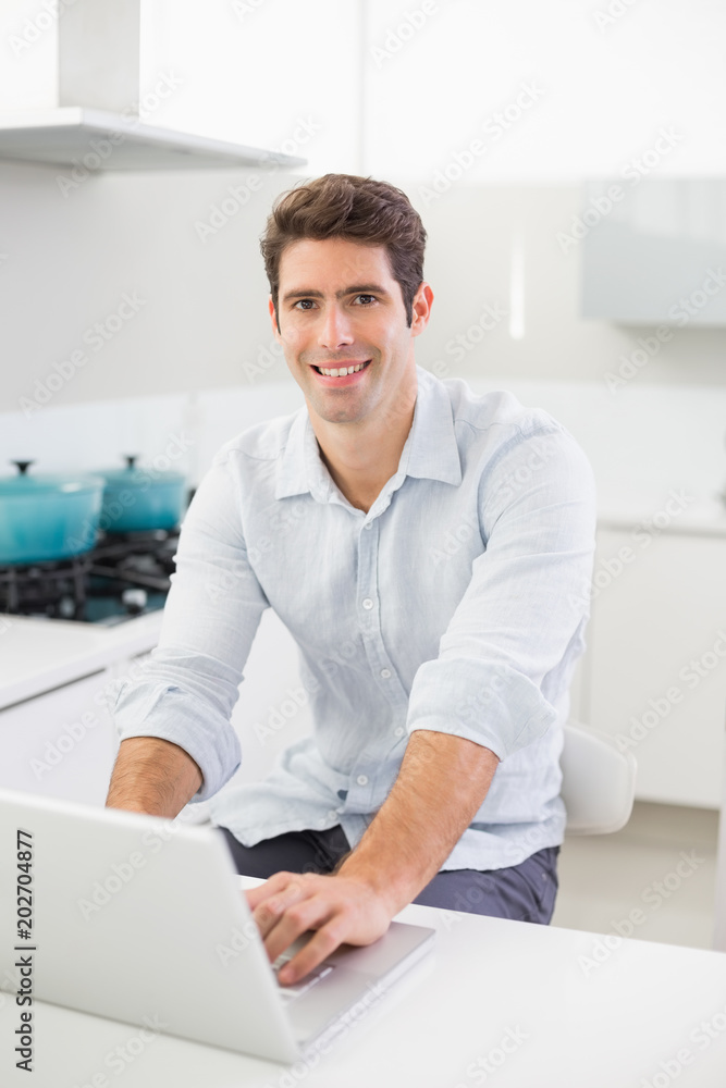 Smiling casual young man using laptop in kitchen Smiling casual young man using laptop in kitchen