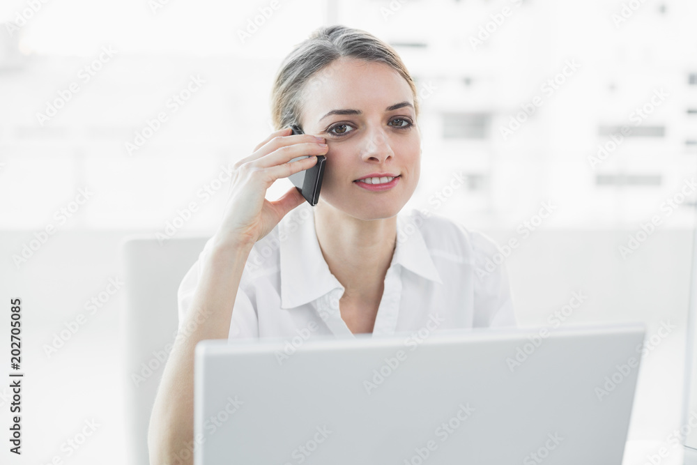 Softly smiling businesswoman sitting at her desk while phoning Softly smiling businesswoman sitting at her desk while phoning