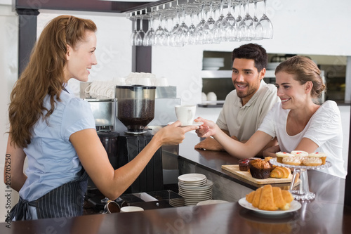 Female waiter giving coffee to a couple at coffee shop