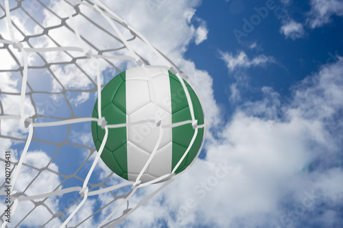 Football in nigeria colours at back of net against bright blue sky with clouds