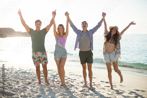 Friends holding hands with arms raised on shore at beach