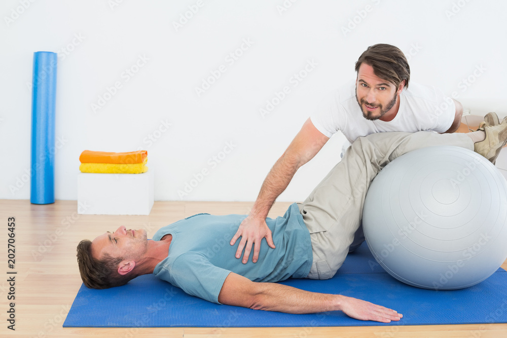 Physical therapist assisting young man with yoga ball Physical therapist assisting young man with yoga ball