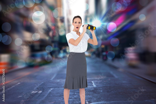 Astonished elegant businesswoman holding binoculars against blurry new york street