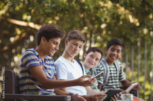 School kids using mobile phone and digital tablet on bench