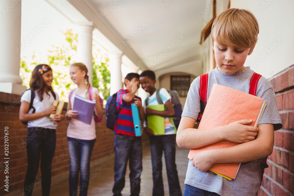 Sad schoolboy with friends in background at school corridor Sad schoolboy with friends in background at school corridor
