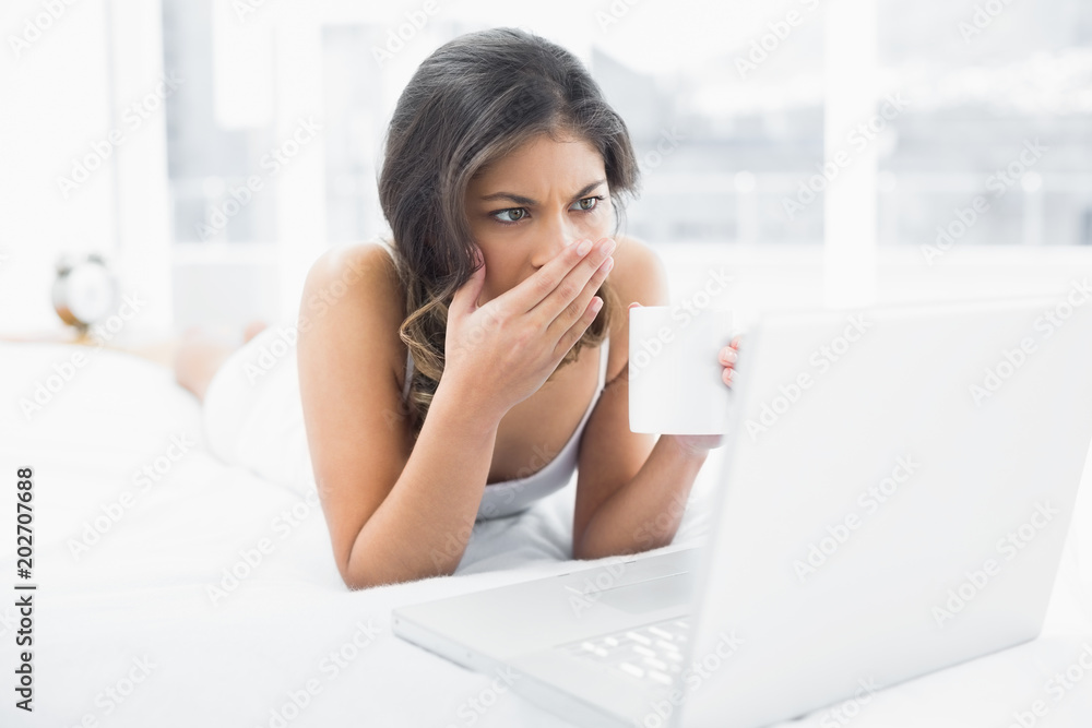 Shocked woman drinking coffee while using laptop in bed Shocked woman drinking coffee while using laptop in bed