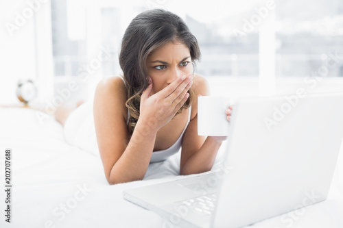 Shocked woman drinking coffee while using laptop in bed © WavebreakmediaMicro