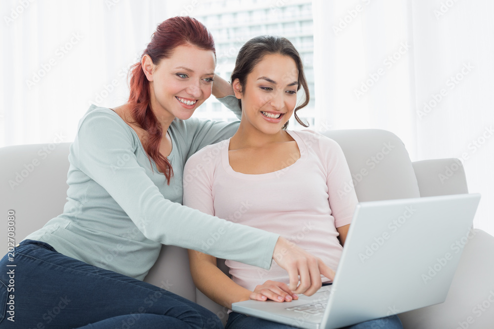 Happy relaxed female friends using laptop at home