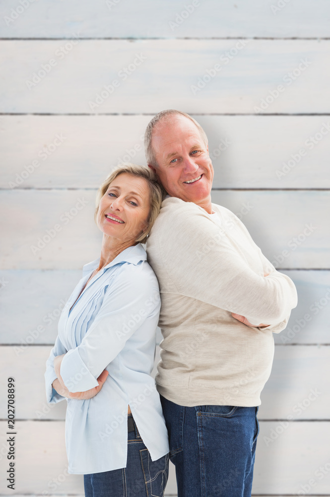 Mature couple standing and smiling at camera against wooden planks Mature couple standing and smiling at camera against wooden planks