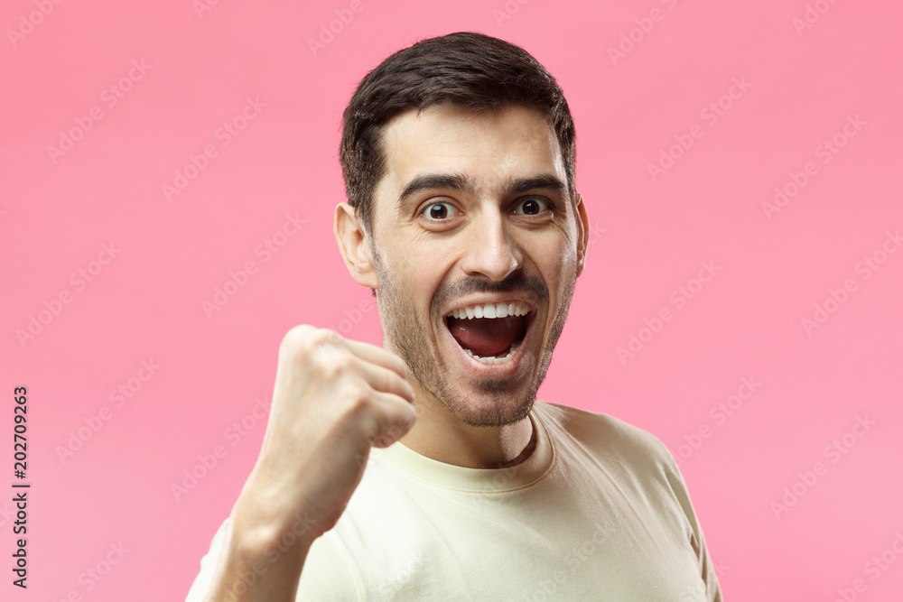 Horizontal portrait of young Caucasian guy pictured isolated on pink background wearing casual T-shirt smiling and laughing in excitement while supporting team or celebrating victory in competition Horizontal portrait of young Caucasian guy pictured isolated on pink background wearing casual T-shirt smiling and laughing in excitement while supporting team or celebrating victory in competition