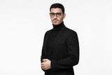 Half-length portrait of young handsome Caucasian guy isolated on white background dressed in black turtleneck, glasses and jacket, looking serious and reserved, ready to answer complicated questions