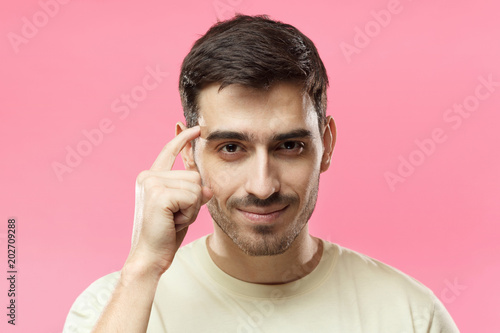 Closeup portrait of young European Caucasian man pictured isolated on pink background pressing finger to temple as if making viewer think more about offer or analyze information better for their good photo