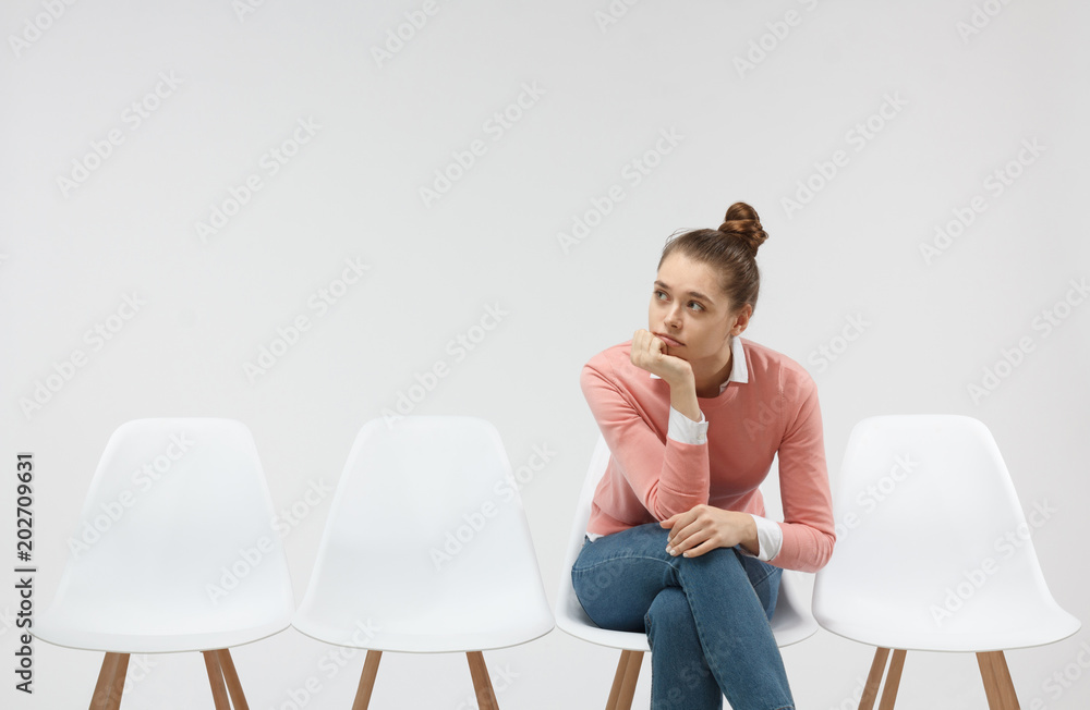 Φωτογραφία Horizontal picture of a young bored female sitting alone in the line and waiting for her turn to come in