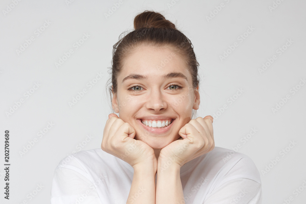 Horizontal headshot of young European Caucasian female pictured isolated on grey background having put chin on fists feeling calm and relaxed listening attentively person she is talking to, smiling Horizontal headshot of young European Caucasian female pictured isolated on grey background having put chin on fists feeling calm and relaxed listening attentively person she is talking to, smiling