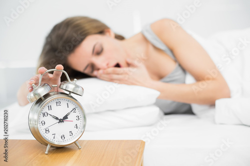 Lovely woman turning off the alarm clock lying on her bed