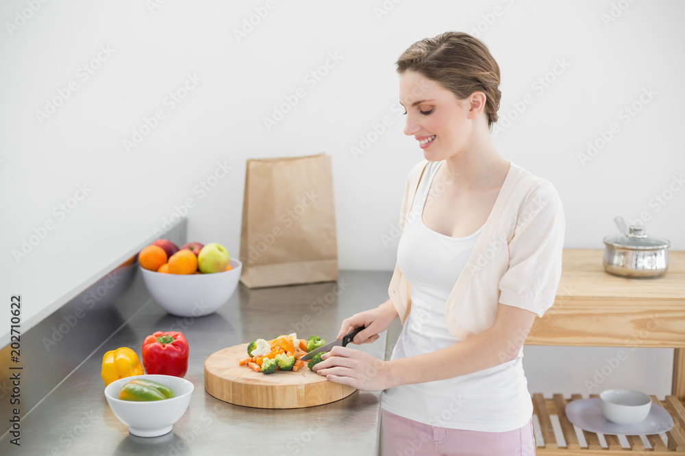 Cheerful young woman cutting vegetables while standing in her kitchen