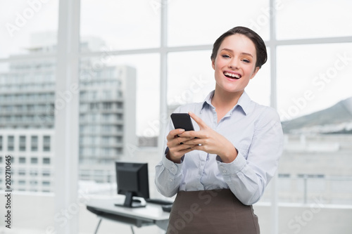 Cheerful businesswoman holding mobile phone in office © WavebreakmediaMicro