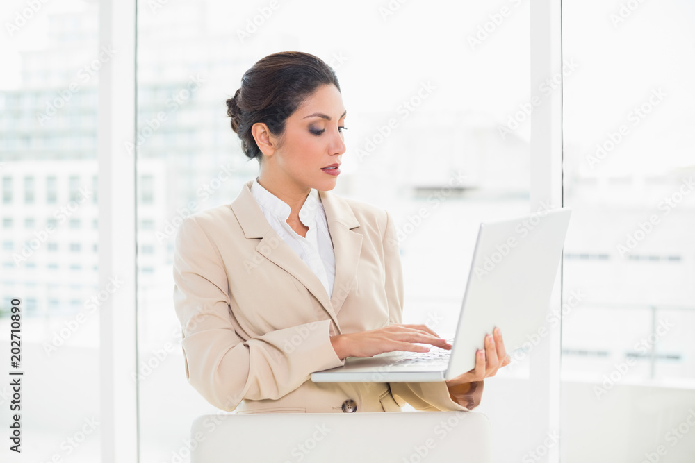 Serious businesswoman standing behind her chair holding laptop Serious businesswoman standing behind her chair holding laptop
