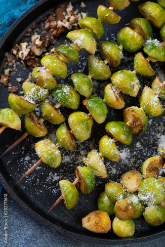 Closeup of wooden skewers with roasted brussels sprouts, grated parmesan and walnuts, view from above