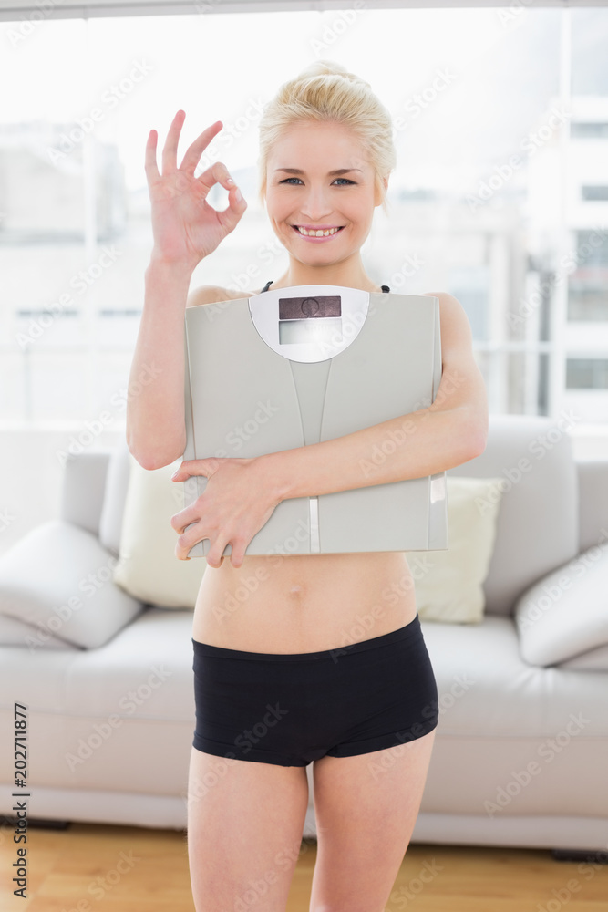 Woman carrying scale while gesturing okay sign