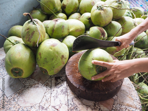 Man using knife to chopped fresh coconut for drink and green coconuts background.