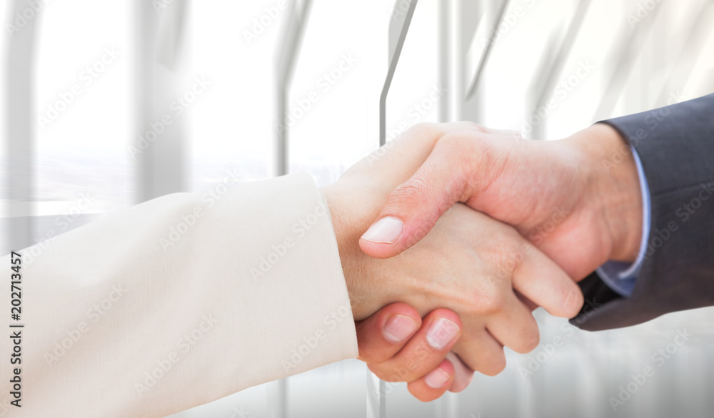 Close up on partners shaking hands against room with large window looking on city Close up on partners shaking hands against room with large window looking on city