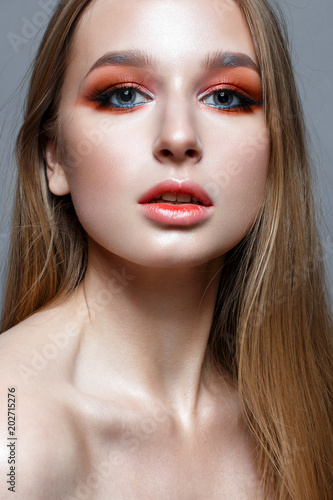 A young girl with long hair and bright creative make-up. Beautiful blond model with shining perfect skin. Beauty of the face. Photo is taken in the studio.