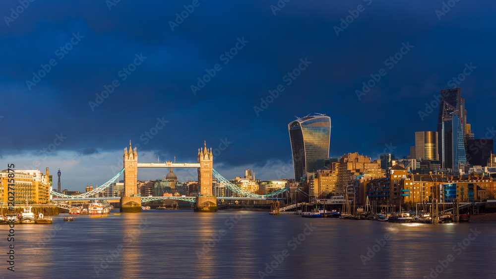 London, England - Beautiful golden sunrise in London with Tower Bridge, St.Paul's Cathedral and skyscrapers of Bank District. Dramatic dark clouds at background