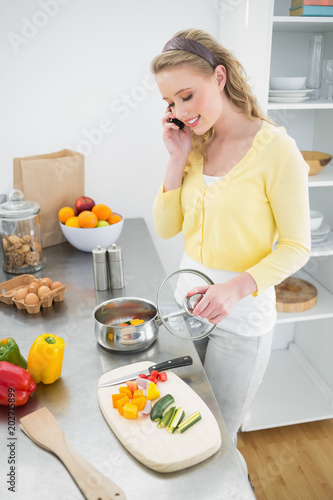 Content cute blonde phoning while preparing a meal