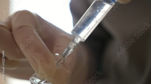 An impressive view of some hands keeping a syringe and an ampule with medicament. Gradually the liquid fills the suringe placed askew in a room photo