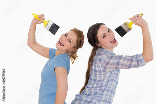 Cheerful female friends singing into paintbrushes