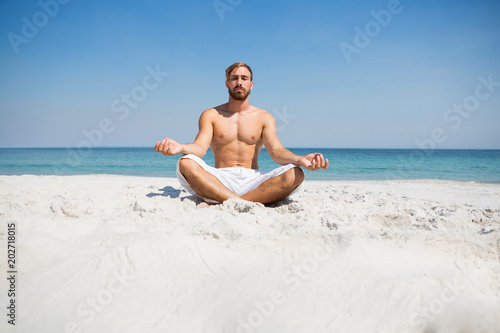 Shirtless man meditating at beach