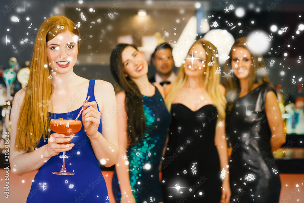 Attractive woman holding cocktail standing in front of her friends against snow falling