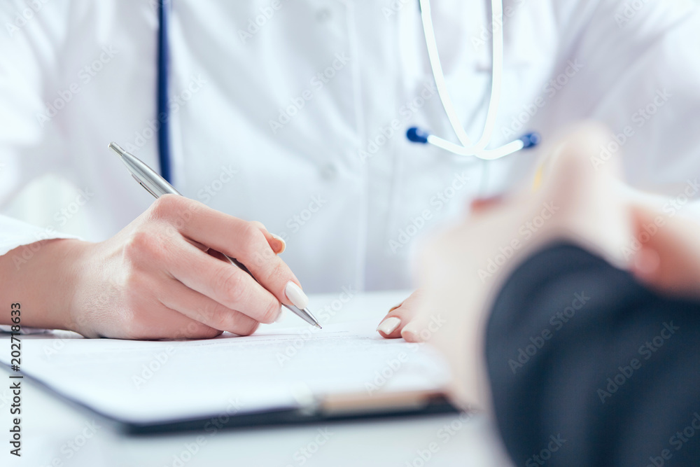 Doctor filling medical form while patient consultation. Patient sitting at doctor office. Doctor filling medical form while patient consultation. Patient sitting at doctor office.