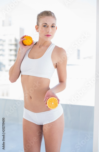 Unsmiling young blonde model holding an orange and a half