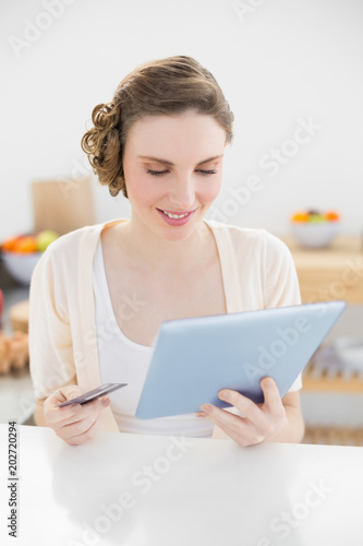 Pretty woman using her tablet for homeshopping while sitting in her kitchen