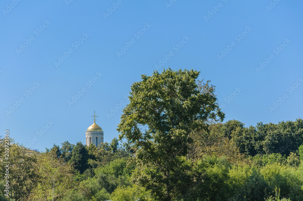 Orthodox Church with Golden dome and a cross rises above the trees on the background of clear blue sky. Vladimir city Orthodox Church with Golden dome and a cross rises above the trees on the background of clear blue sky. Vladimir city