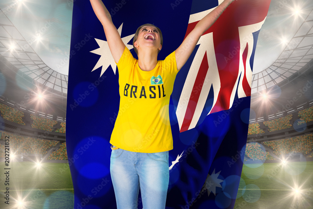 Excited football fan in brasil tshirt holding australia flag against large football stadium with lights