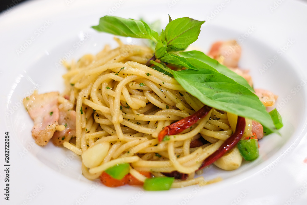 The spaghetti spicy bacon and ham with basil, tomato, black pepper, lettuce and paprika on white dish set on table for food background or texture - homemade food concept.