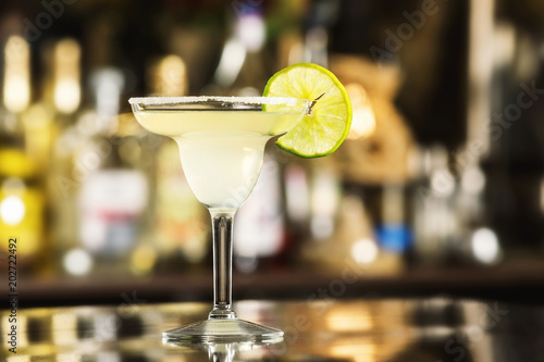Closeup glass of margarita cocktail decorated with lime at bar background.